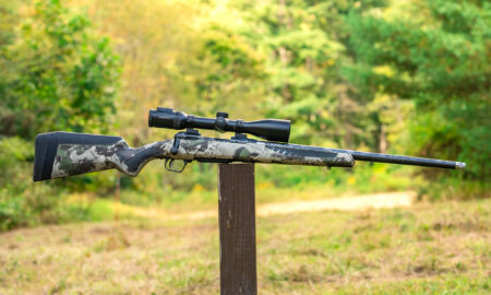 The new Savage 110 Ultralite Camo bolt-action rifle balanced on a post in a field.