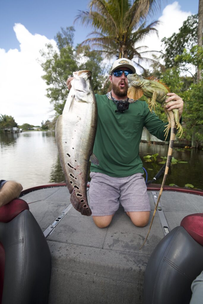 A person holds a clown knifefish and an iguana on a boat.