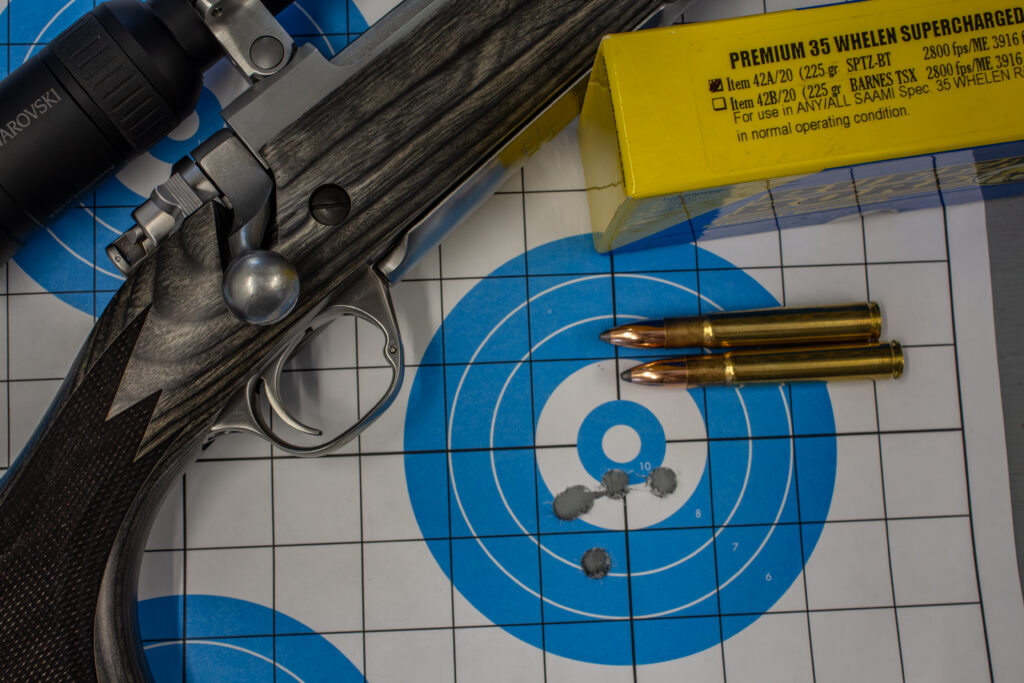 A target showing 5 bullets holes, with rifle and ammo nearby.