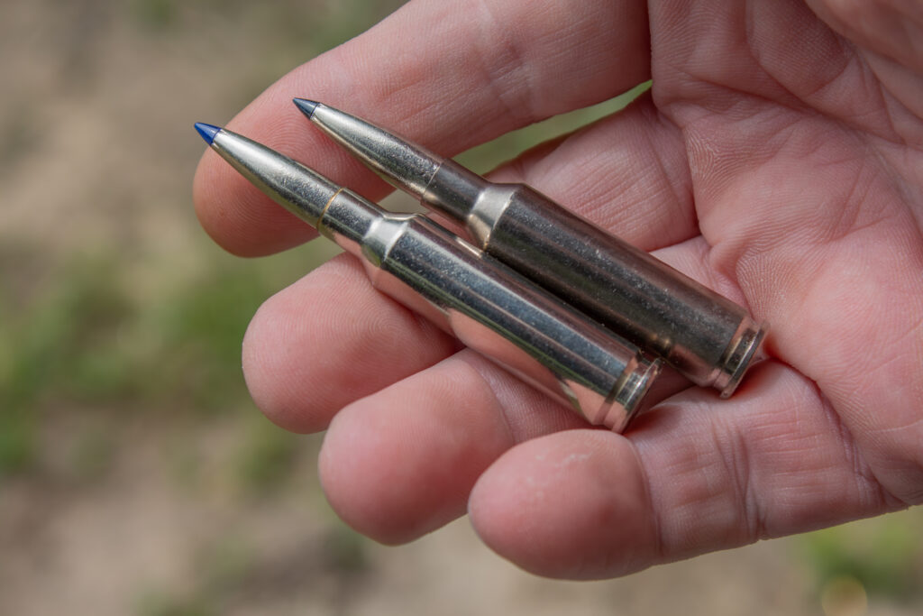 A hand shows a 6.5 Creedmoor +PEAK cartridge next to a standard 6.5 Creedmoor round.
