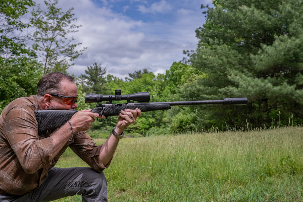 A man shoots the new Weatherby Mark V Backcountry Guide Ti rifle from the kneeling position in a field.