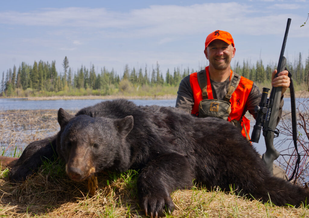A hunter with a rifle poses with a black bear. 