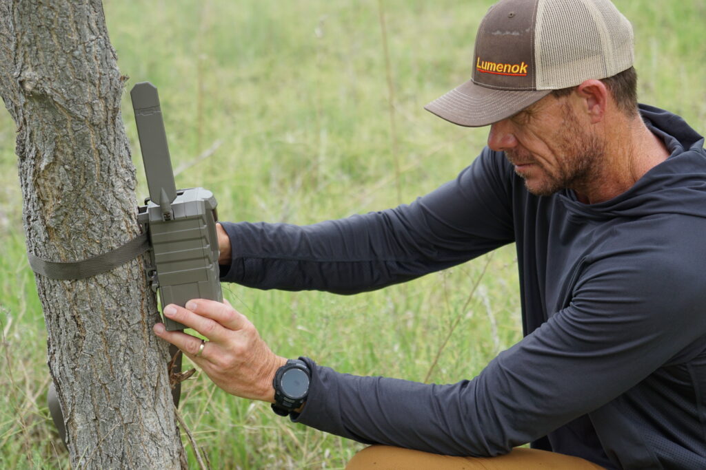 A person sets up a Tactacam Reveal 4.0 Pro camera on a tree