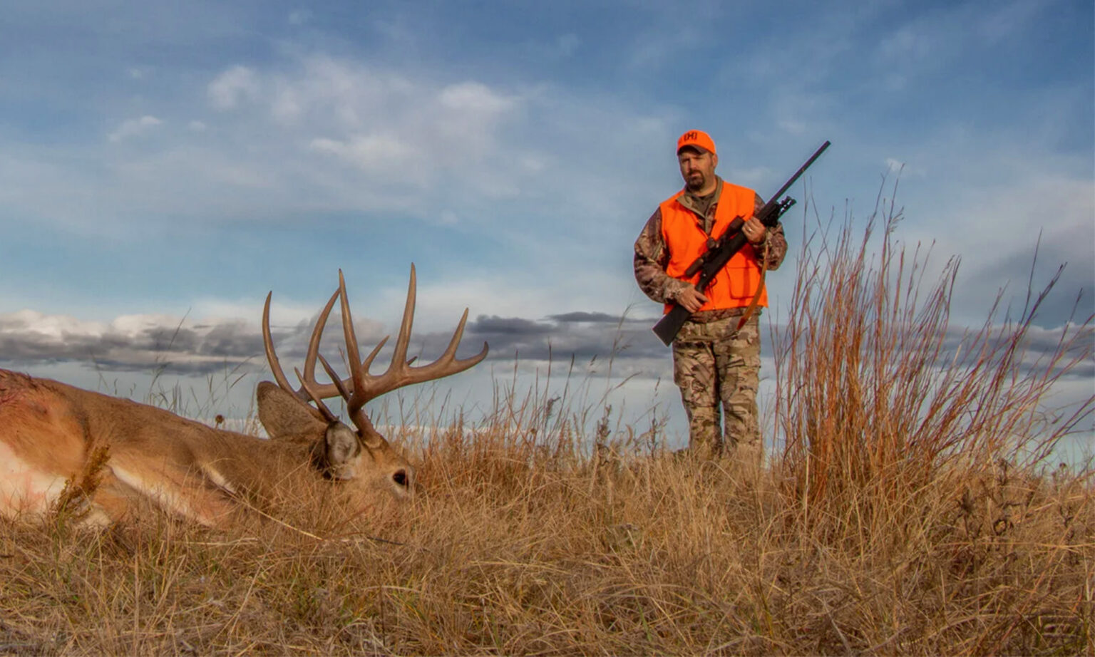 A hunter with a rifle approaches a whitetail buck he shot
