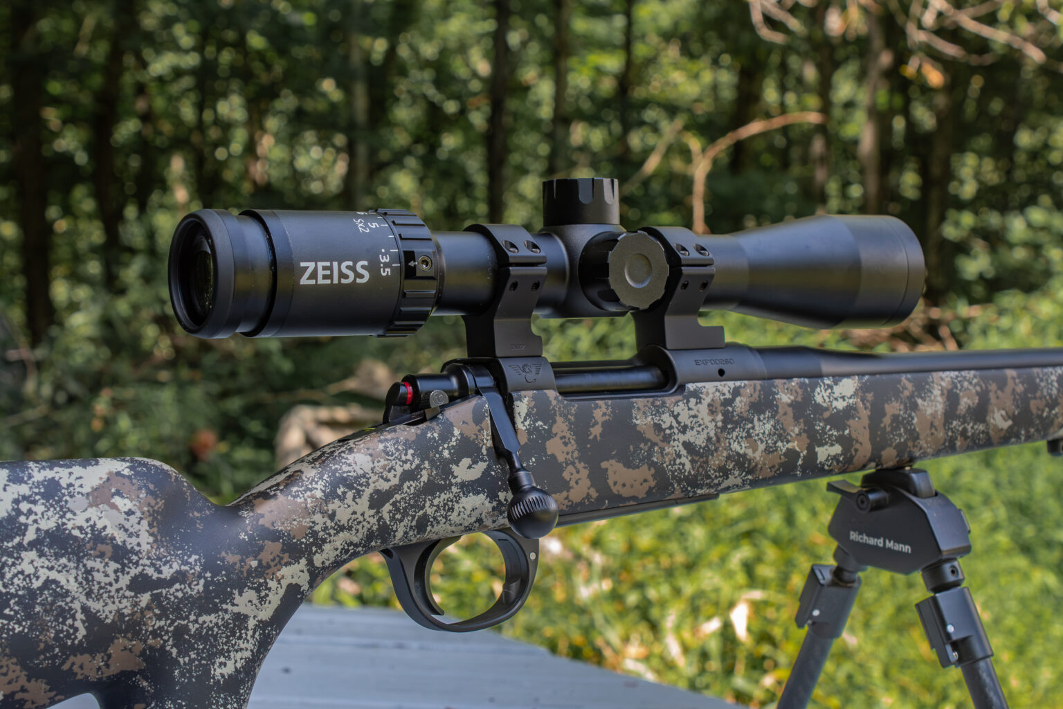 A black riflescope on top of a camo colored bolt action rifle