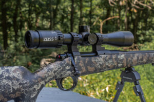 A black riflescope on top of a camo colored bolt action rifle