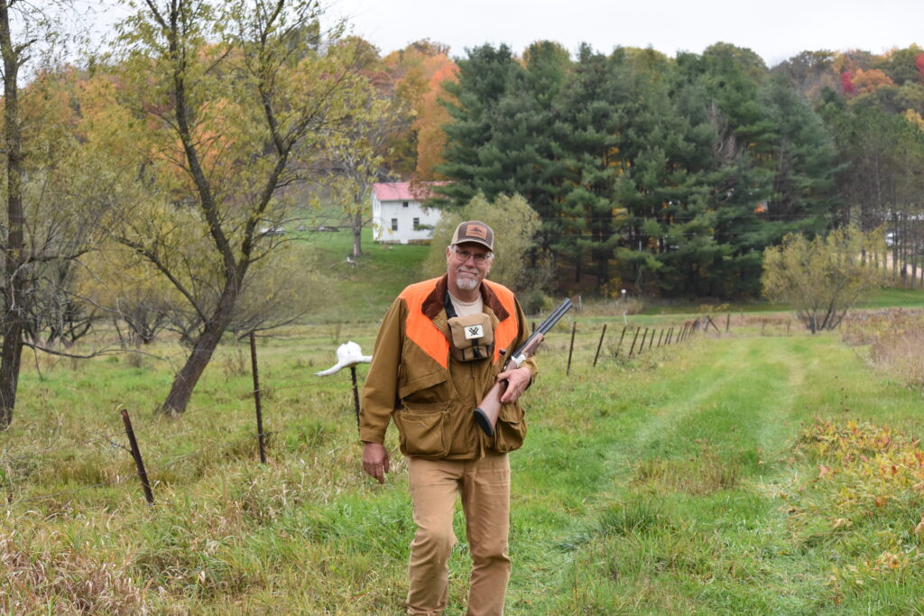 A hunter poses with a shotgun on his farm.