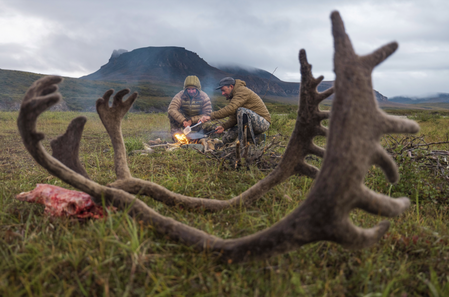 Two hunters cooking after a successful caribou hunt in Alaska.
