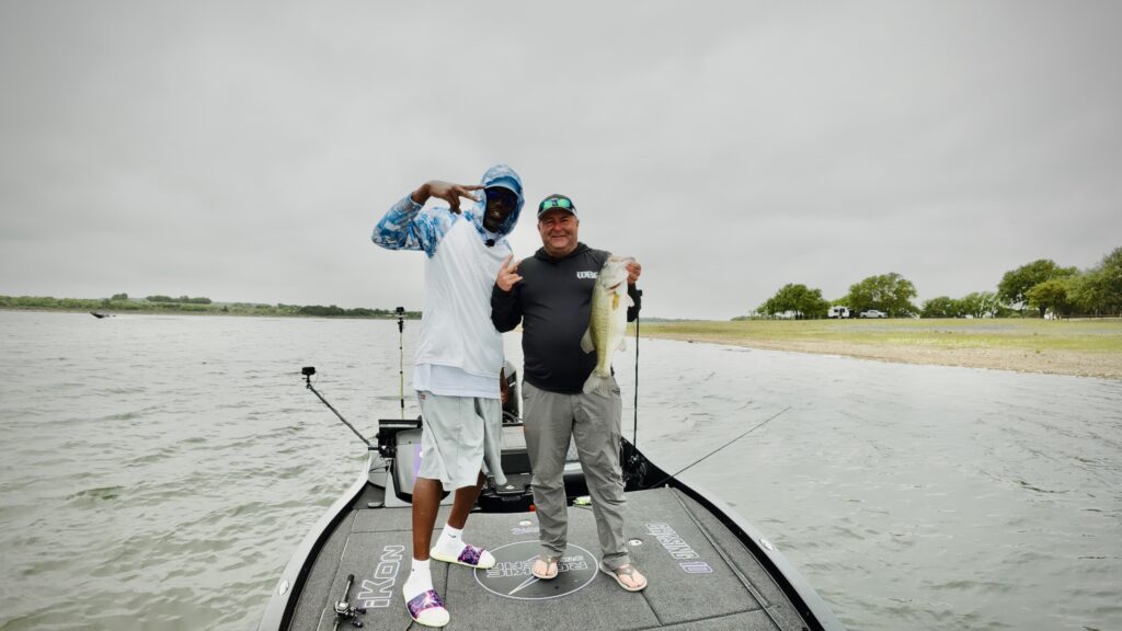 The Biggest Bass Fishing Tournament Ever Is About to Begin Two fishermen stand on a fishing boat. One is holding a large bass