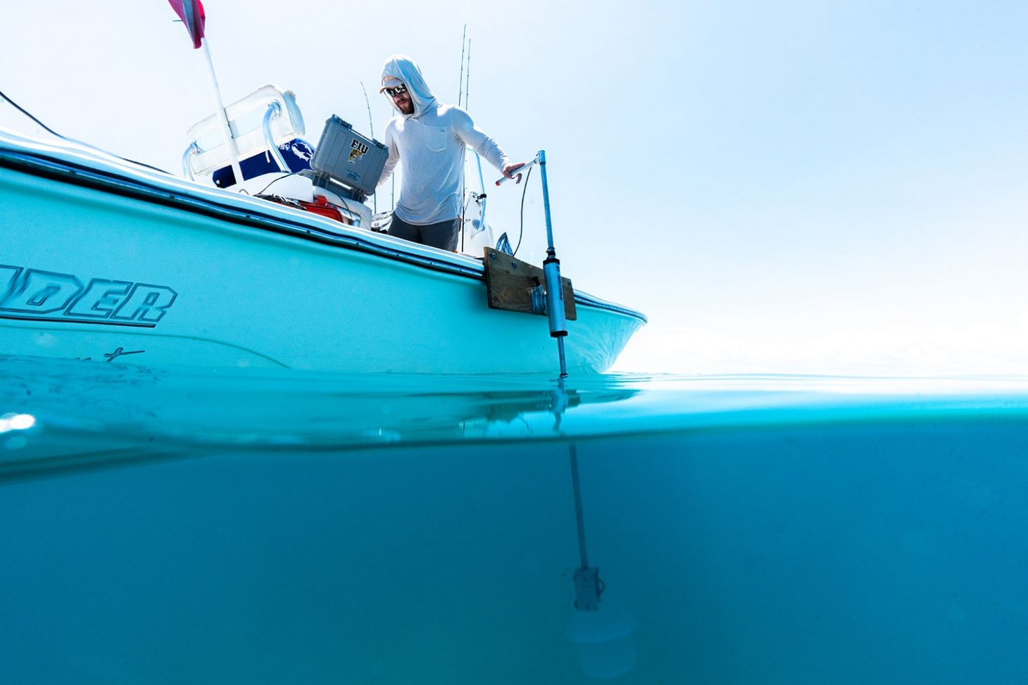 researcher on boat has hand on top of hydrophone, which stretches down into water below boat