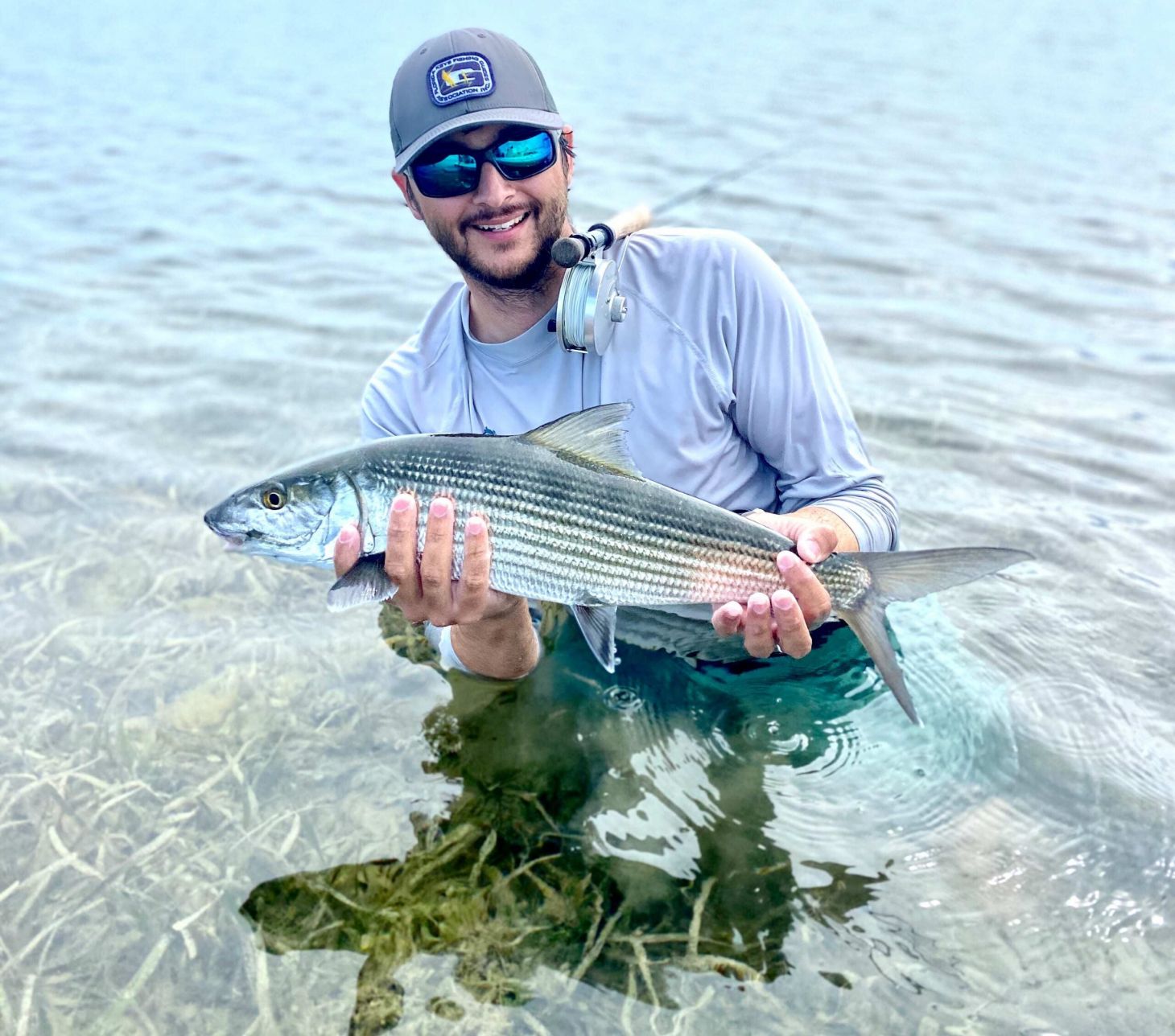 guide nick castillo stands in water and holds up a bonefish as he balances his fly rod over his shoulder