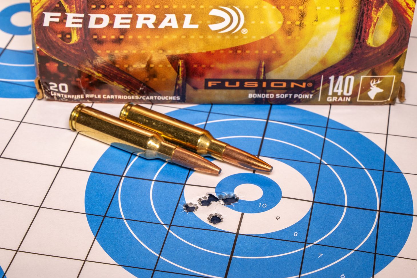 A rifle target showing a group of bullet holes with ammo resting on the target. 