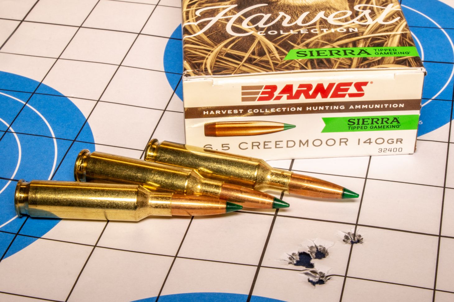 A rifle target with five bullet holes in it, with a box of ammo and three loose cartridges. 