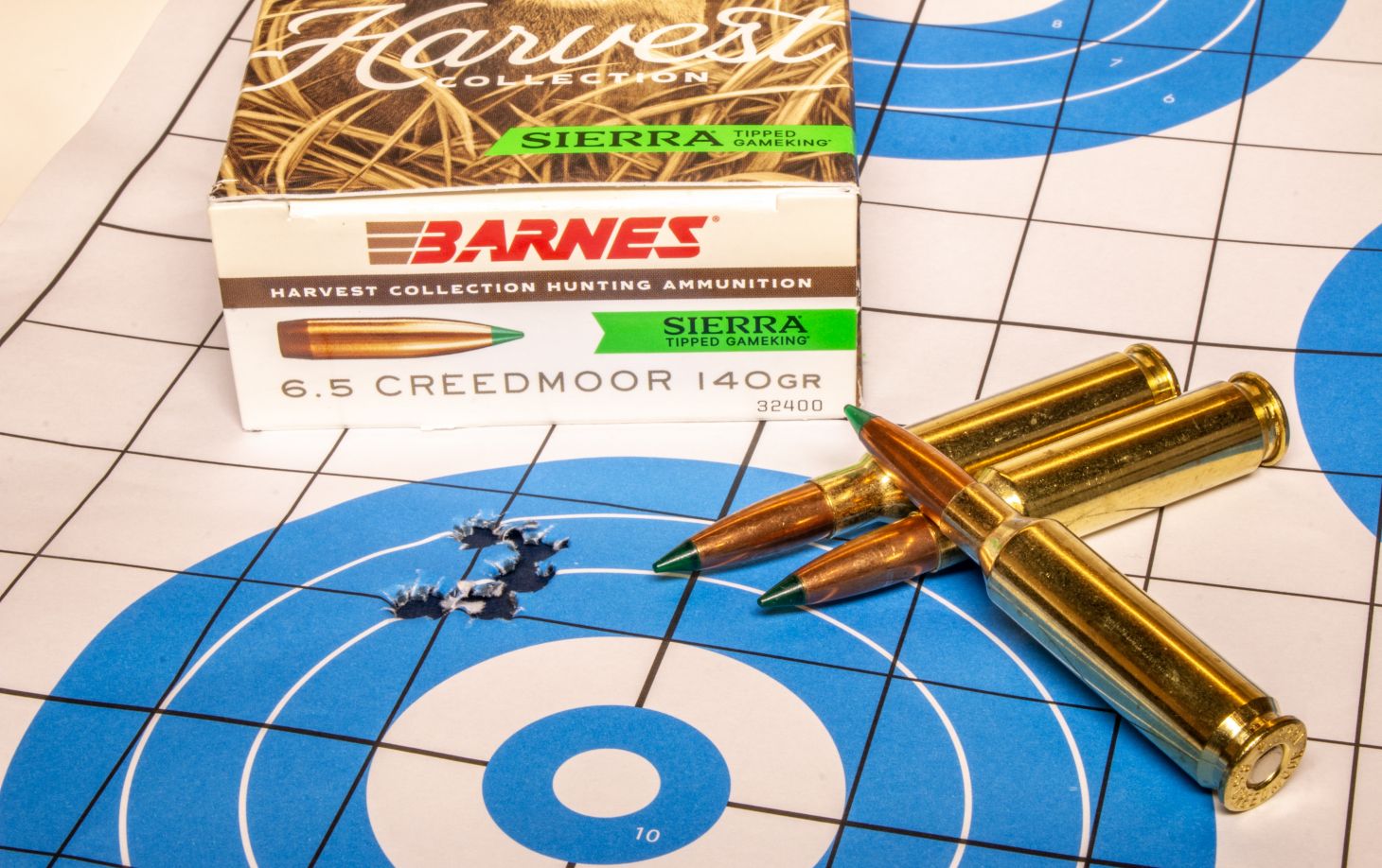 A rifle target with five bullet holes in it, with a box of ammo and three loose cartridges. 