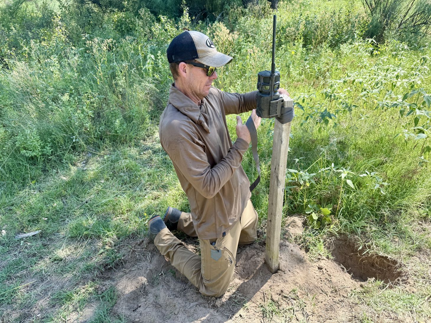 A man sets up a trail camera in a field. 