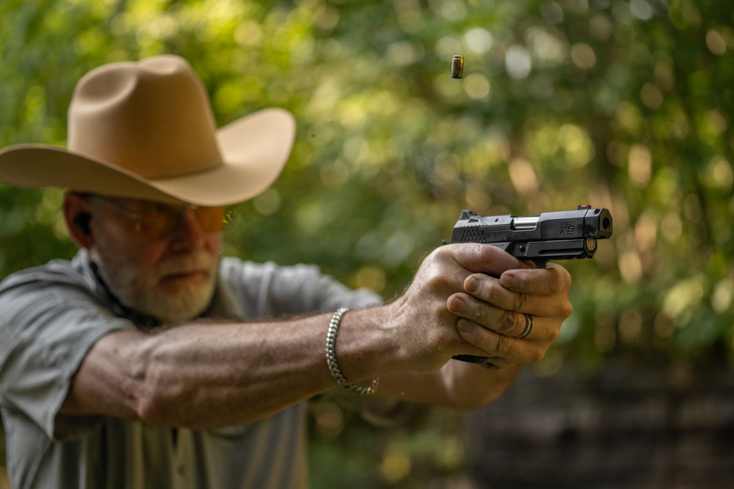 A shooter in plaid shirt and green jacket grips a 9mm handgun on the range.