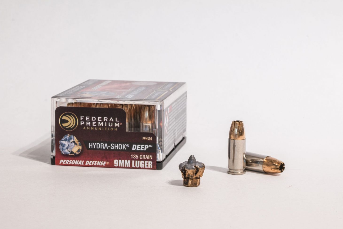Box of 9mm Luger ammo with one fired bullet and two loose cartridges on white background