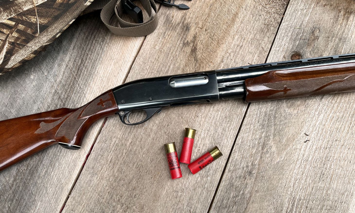 A Remington 870 on barn boards with three shotgun shells.