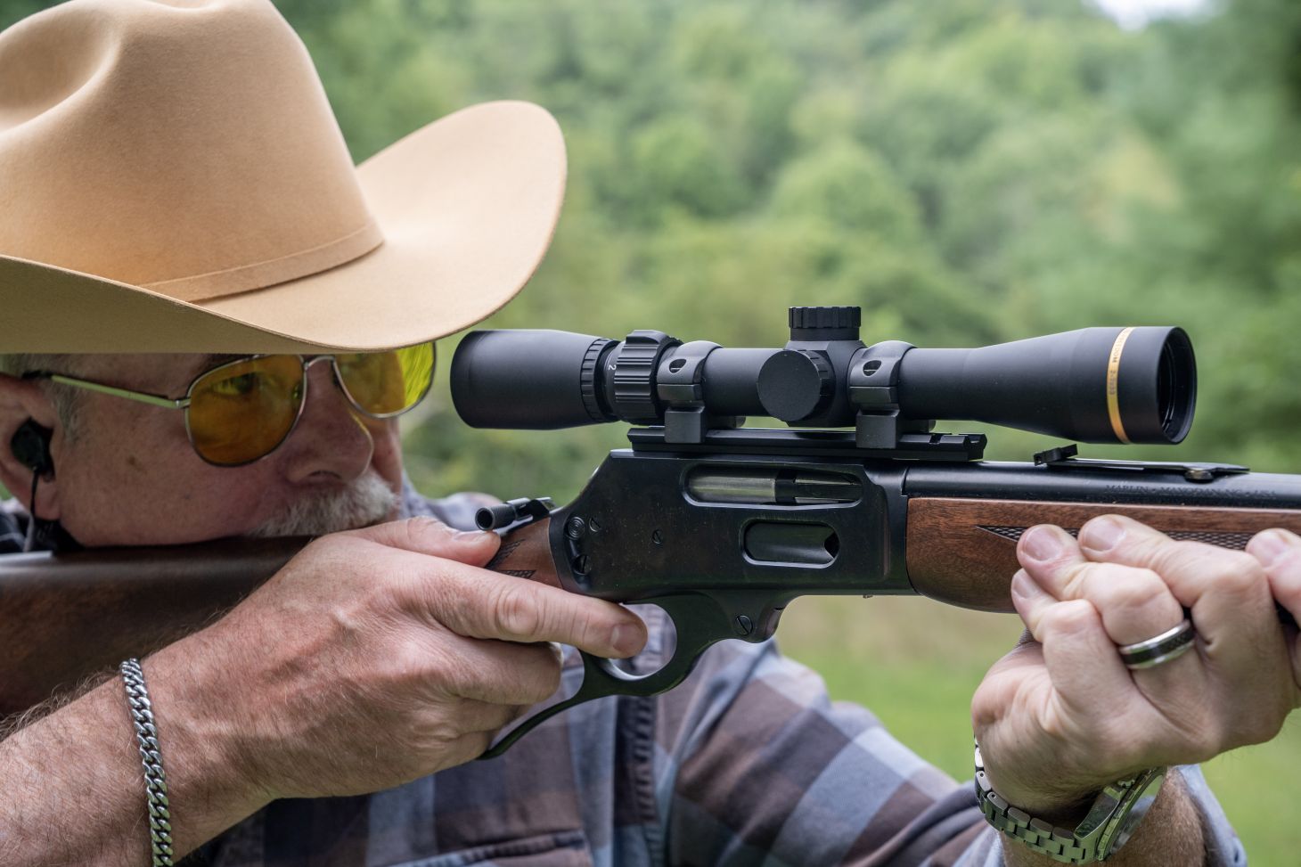 A shooter in a cowboy hat fires a scoped lever-action rifle. 