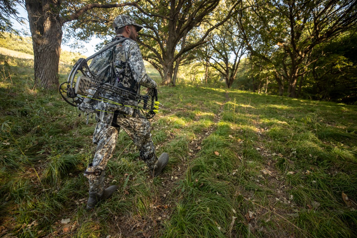 A bowhunter walk a trail through the woods. 