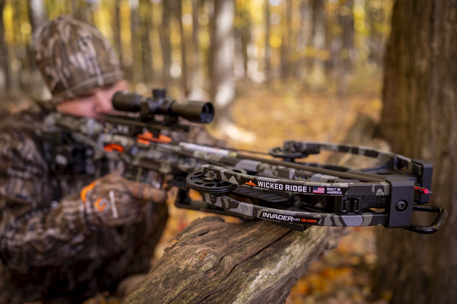 A shooter aims the new Wicked Ridge Invader M-1 De-Cock crossbow over a log in the woods.
