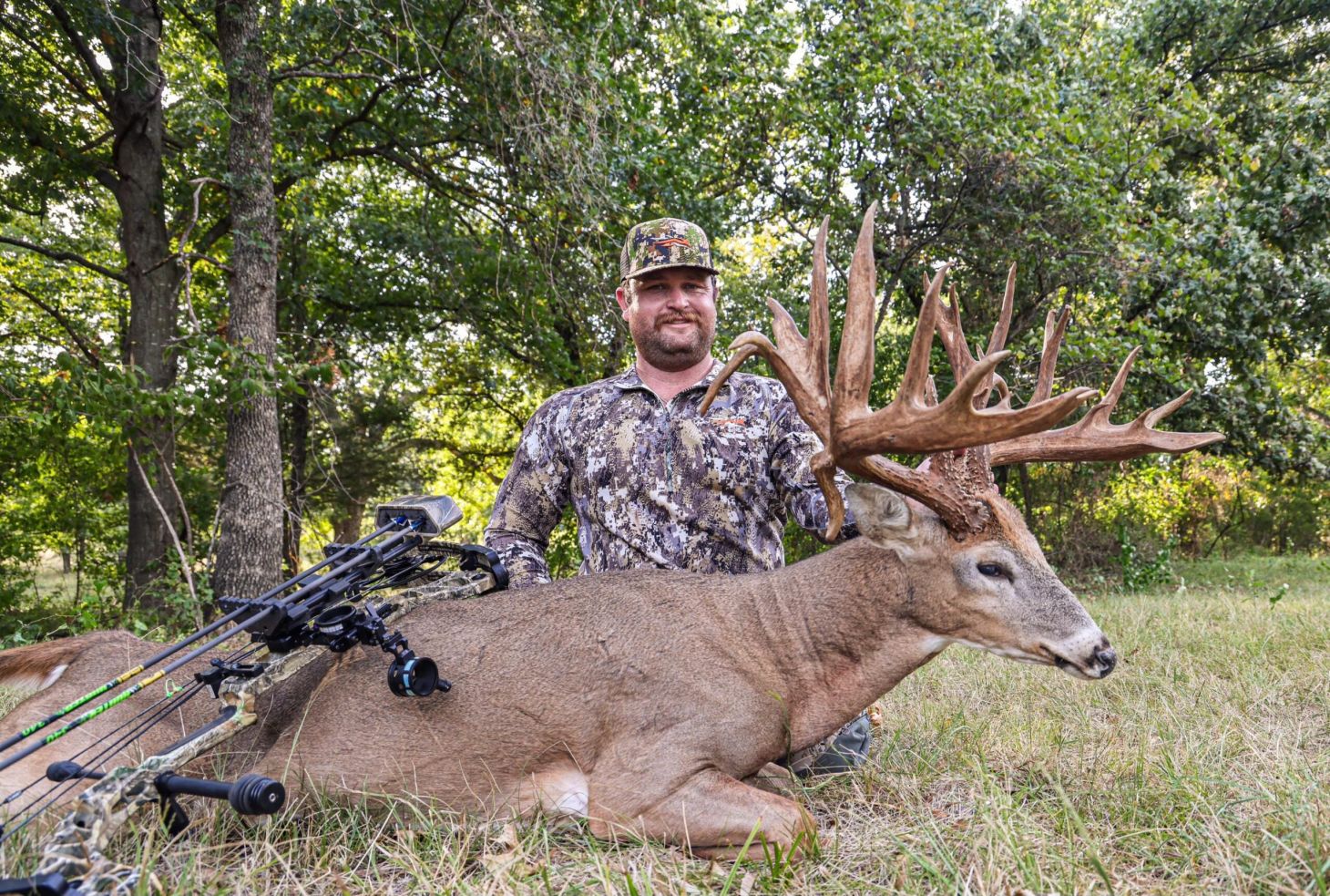 An Oklahoma bowhunter sits on the ground posing with a 200-class nontypical whitetail buck.