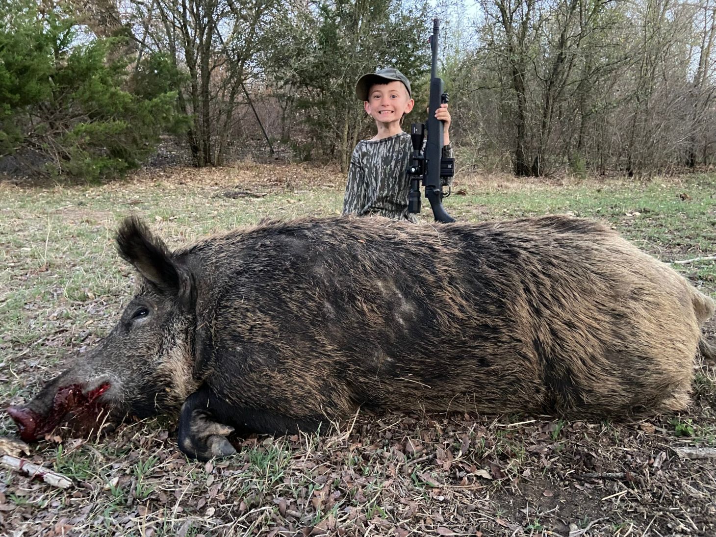 Child standing over giant boar shot with 300 blackout ammo and rifle