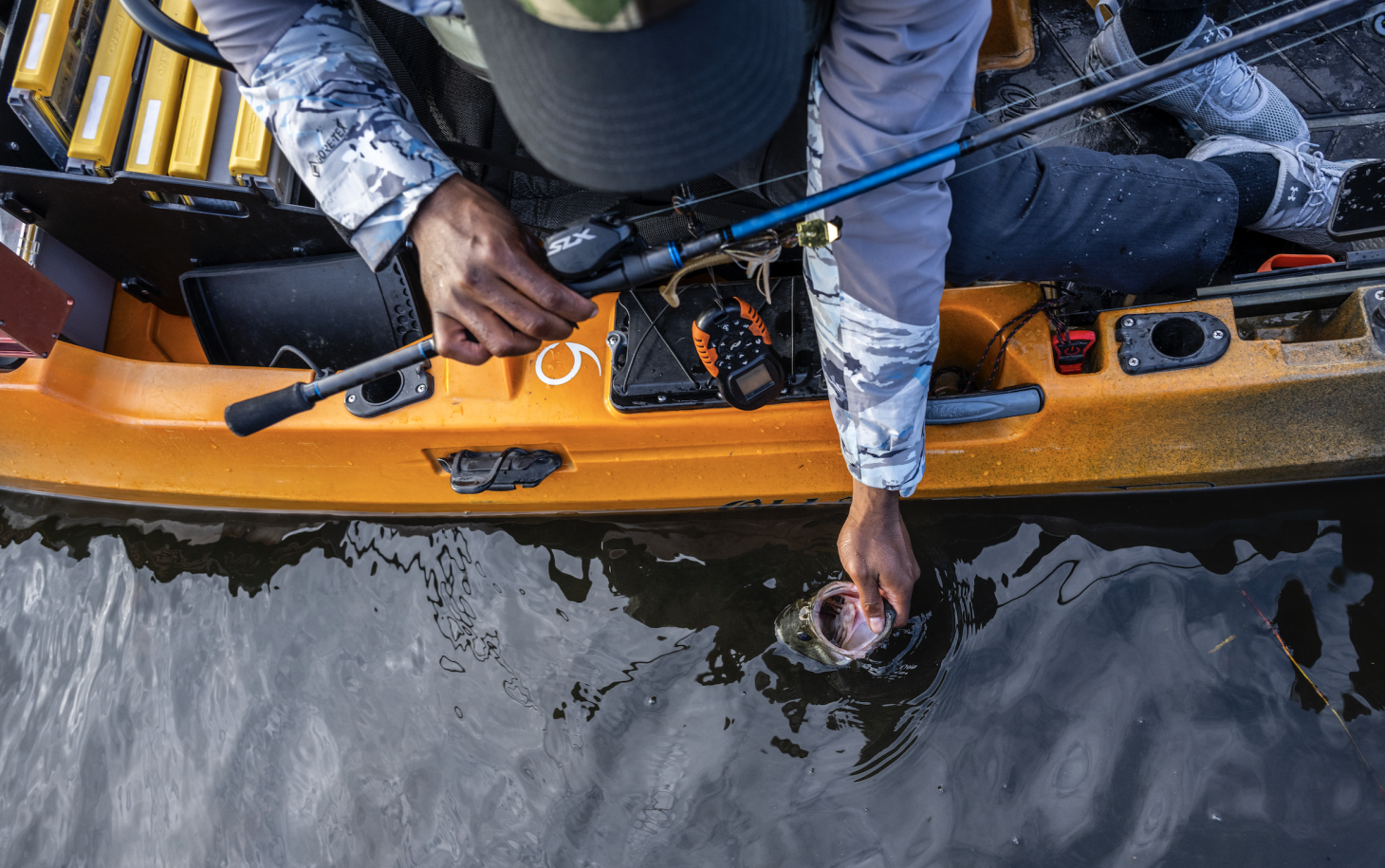 Angler holding bass in water next to kayak