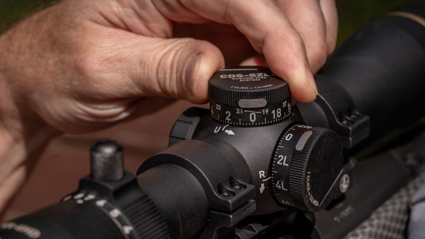 A shooter's hand adjusts the CDS elevation turret on a Leupold VX-6HD Gen 2 scope. 