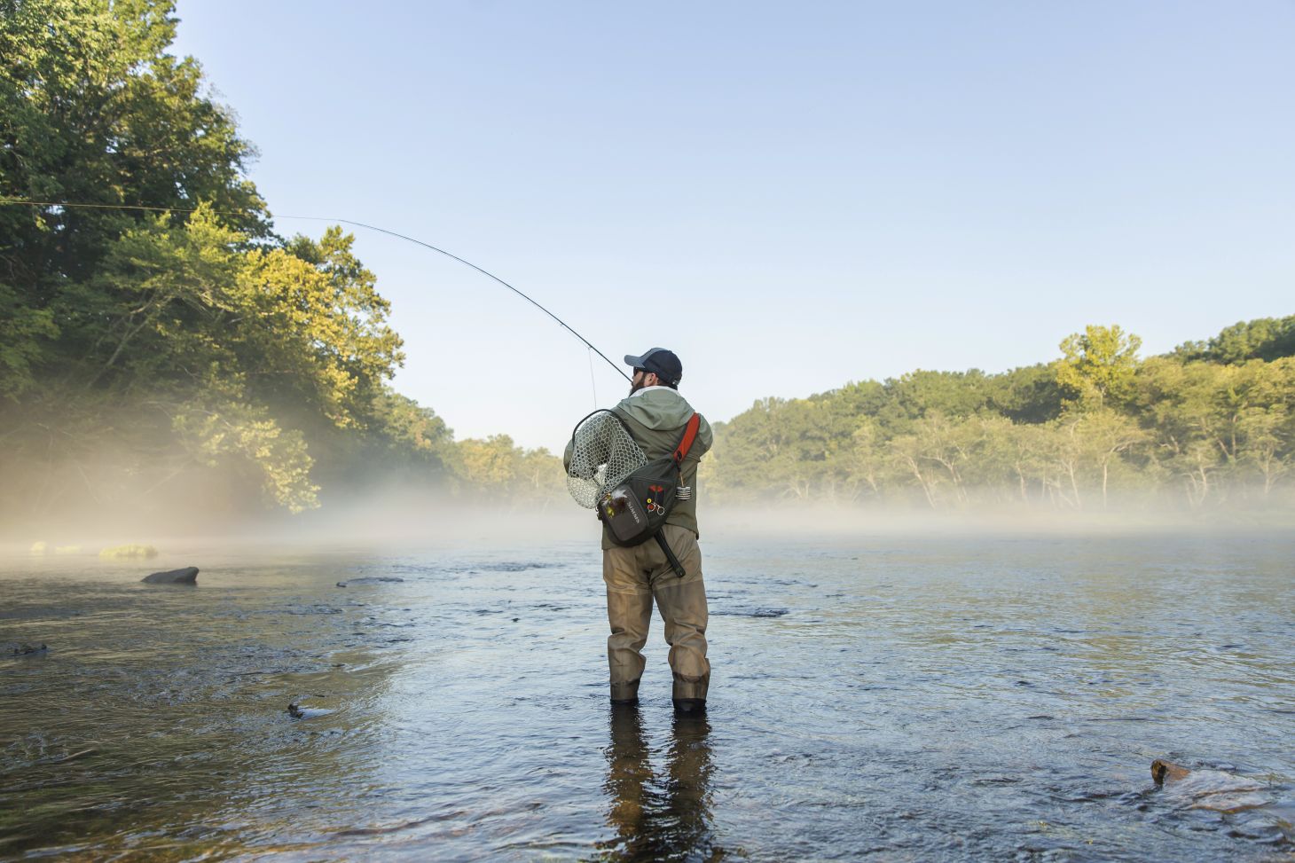 A fly fisherman casts on a river with fog on the surface
