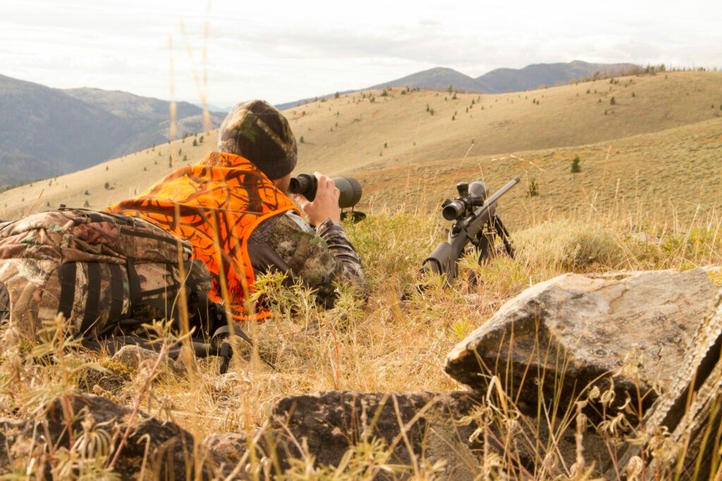Man with rifle looking through spotting scope.