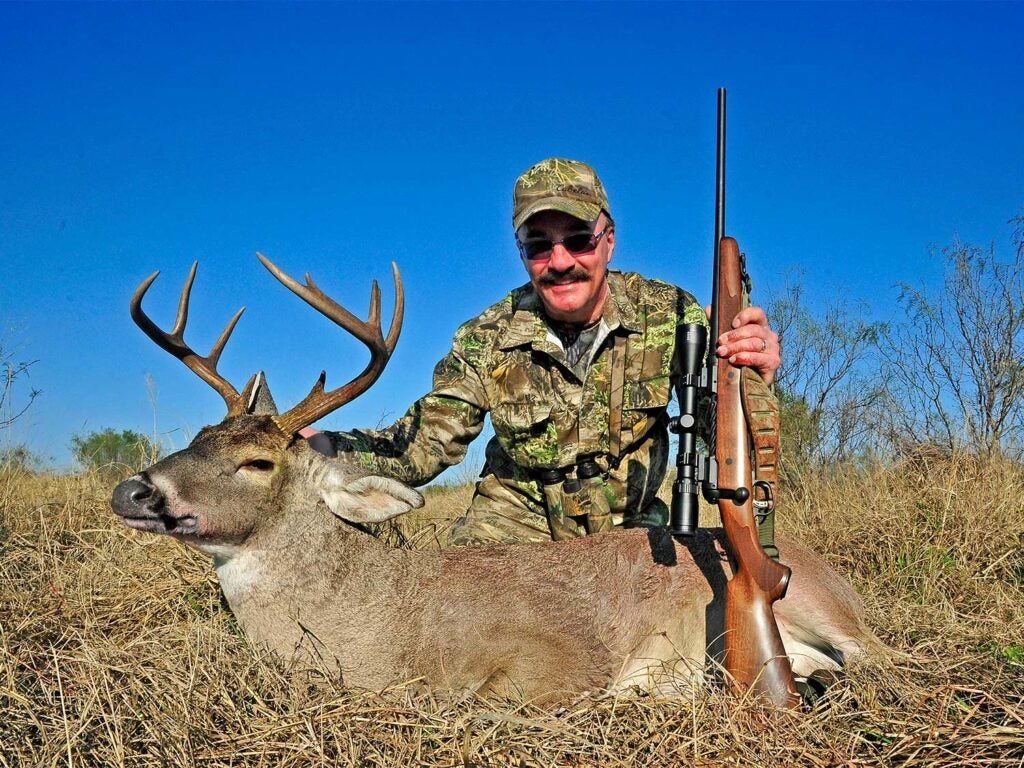 hunter kneeling behind a buck while holding a savage rifle
