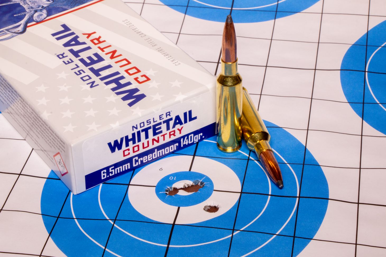 The new Nosler Whitetail Country ammo lying on top of a rifle target with five bullet holes. 