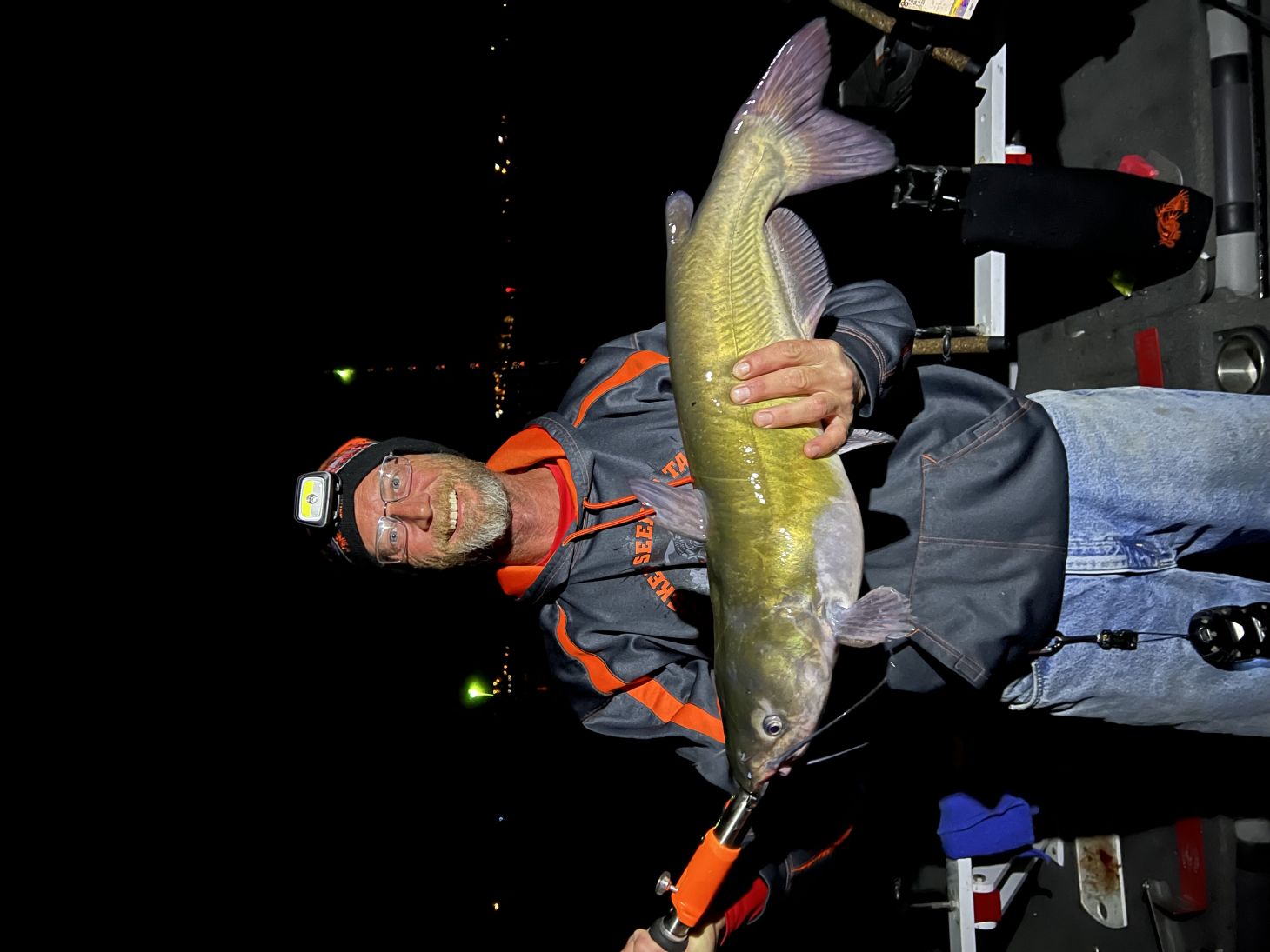 Angler holding up catfish on boat at night.