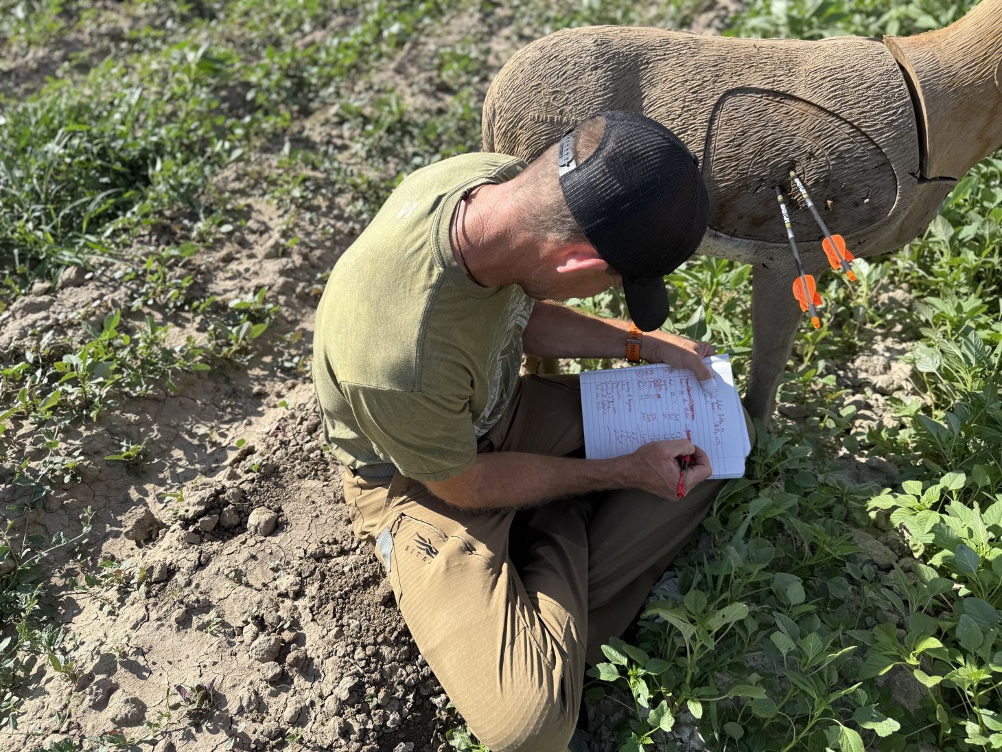 A person writes in a notebook while sitting next to a 3D archery deer target.