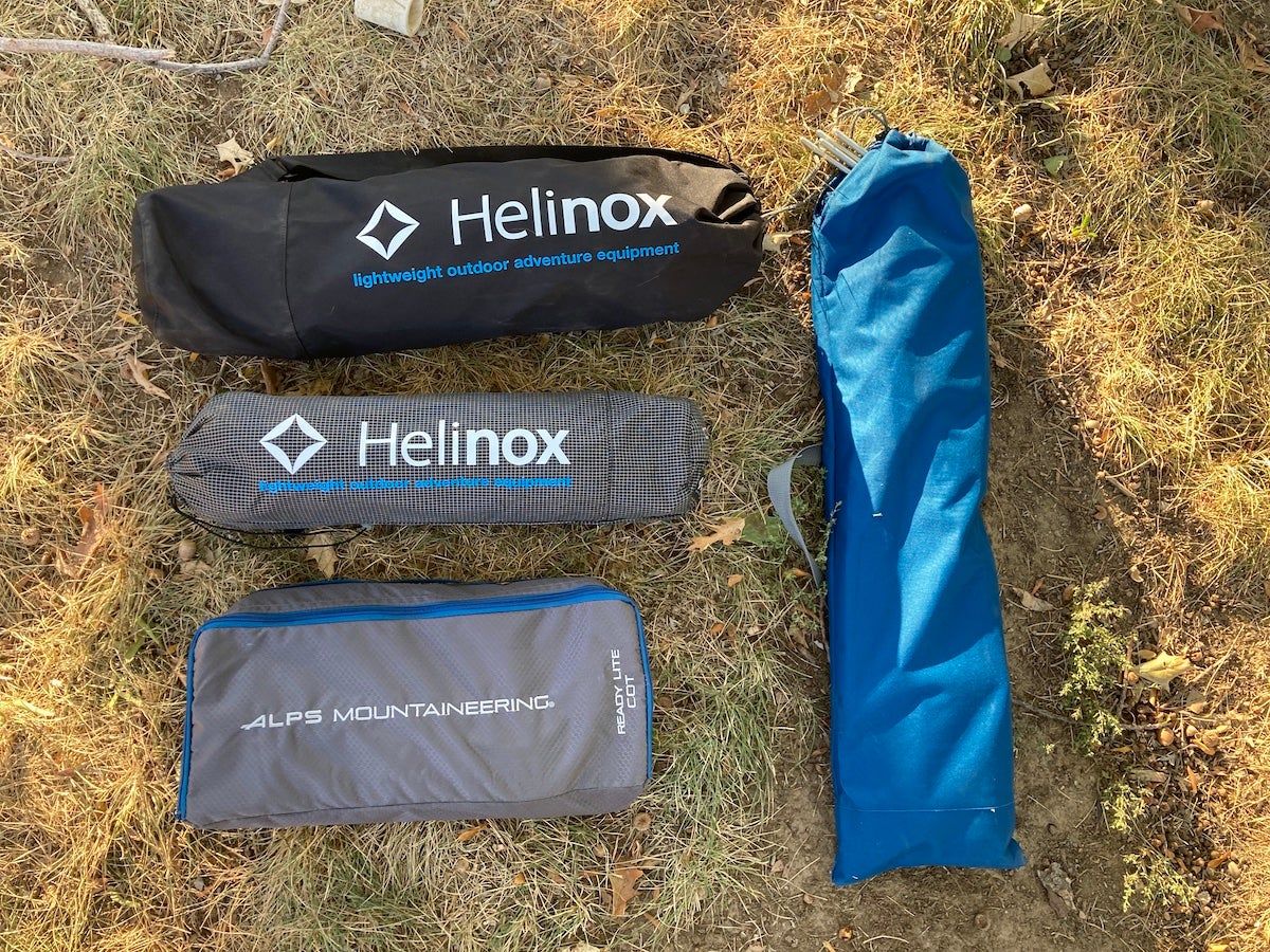 Camping cots packed down in carrying bags on the grass during testing