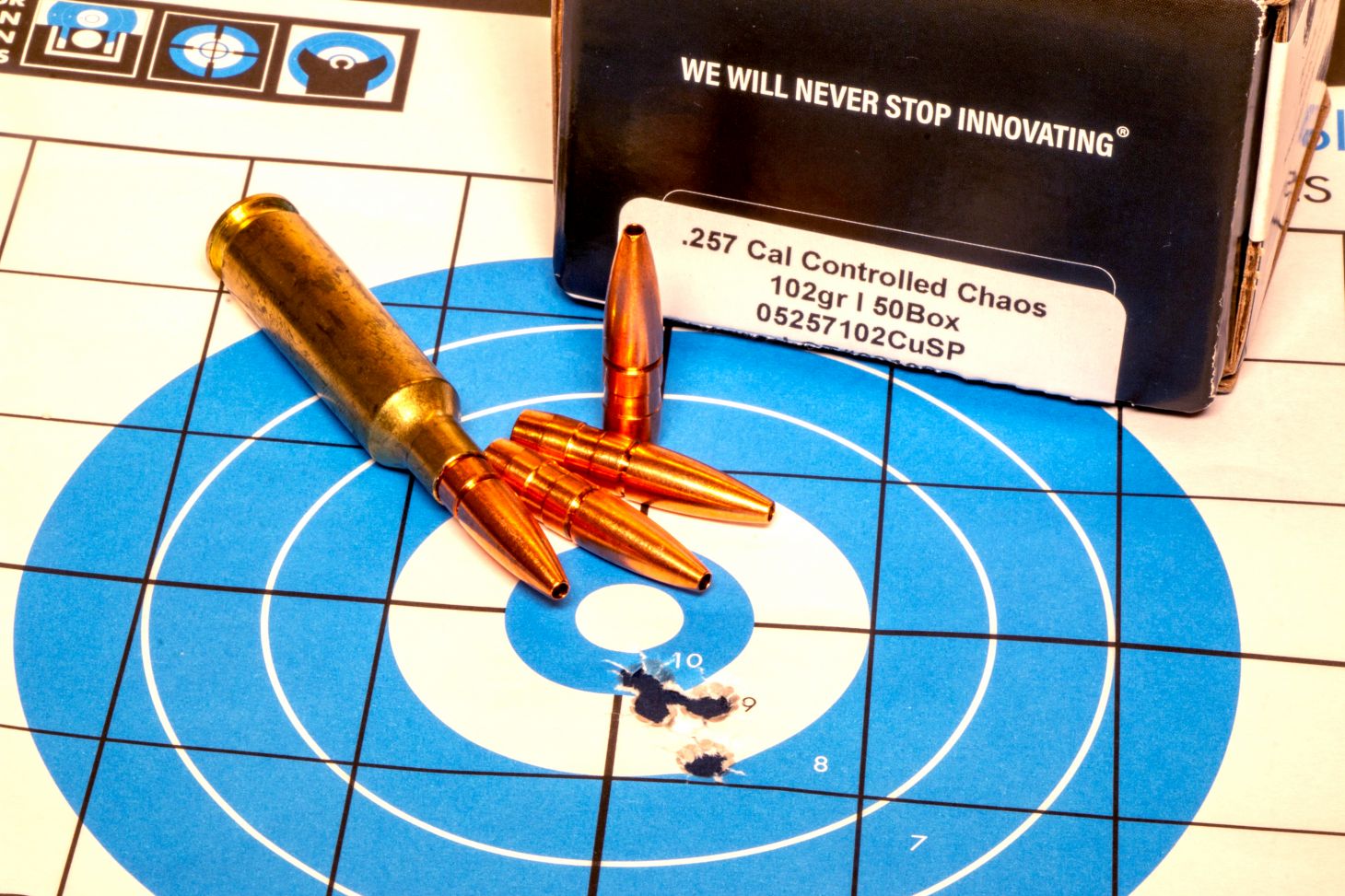 A rifle target with five bullet holes in it and ammo lying on top. 