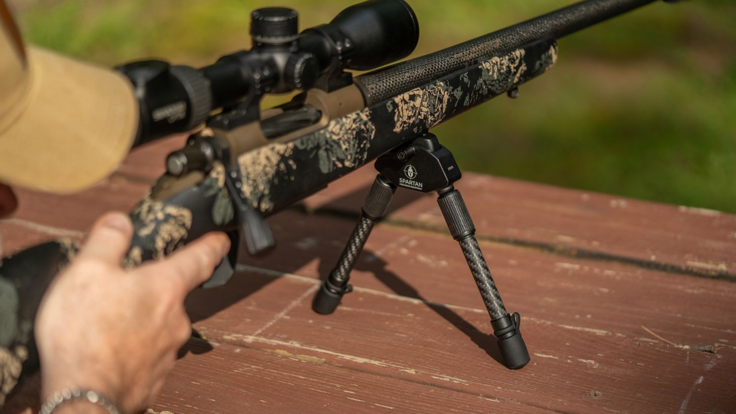 A man shoots a rifle from a bench rest, using a bipod for support. 