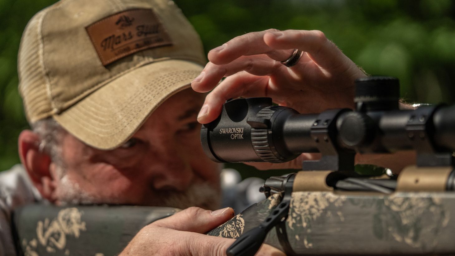 A man shooting from a bench rest adjusts the focus on his riflescope. 