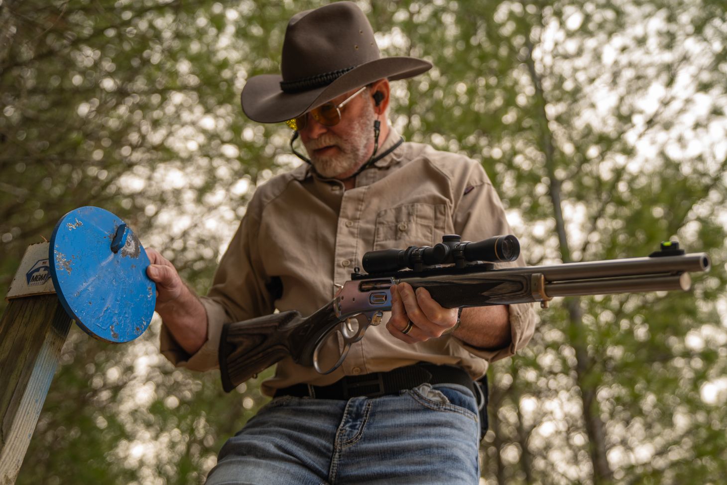 A shooter holding a lever-action rifle check a steel target in the woods. 