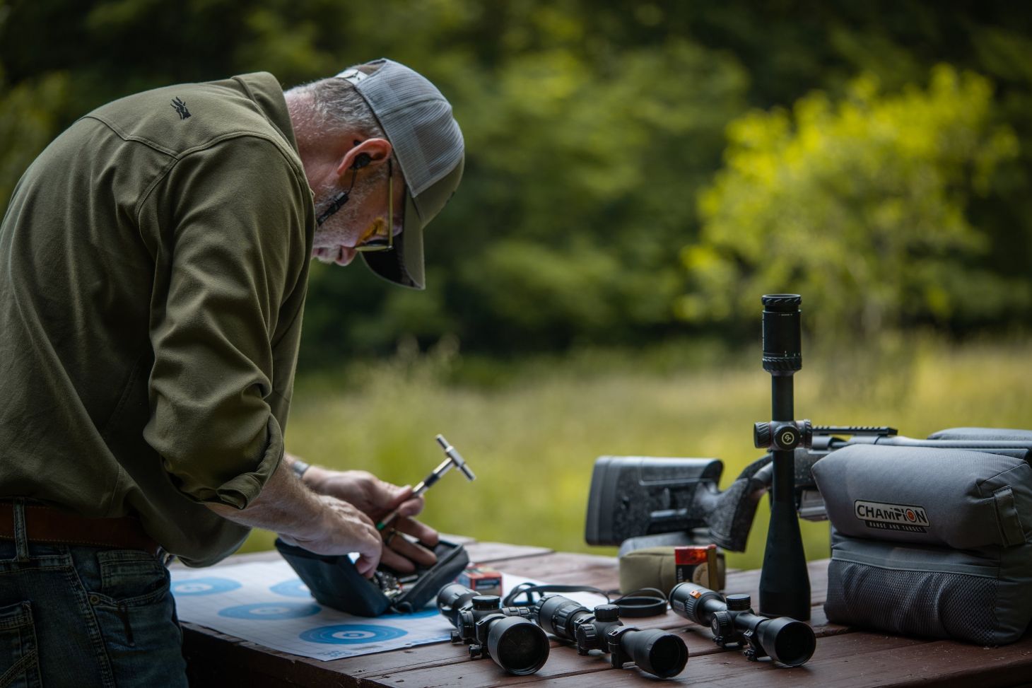 Man measuring a riflescope on a bench.