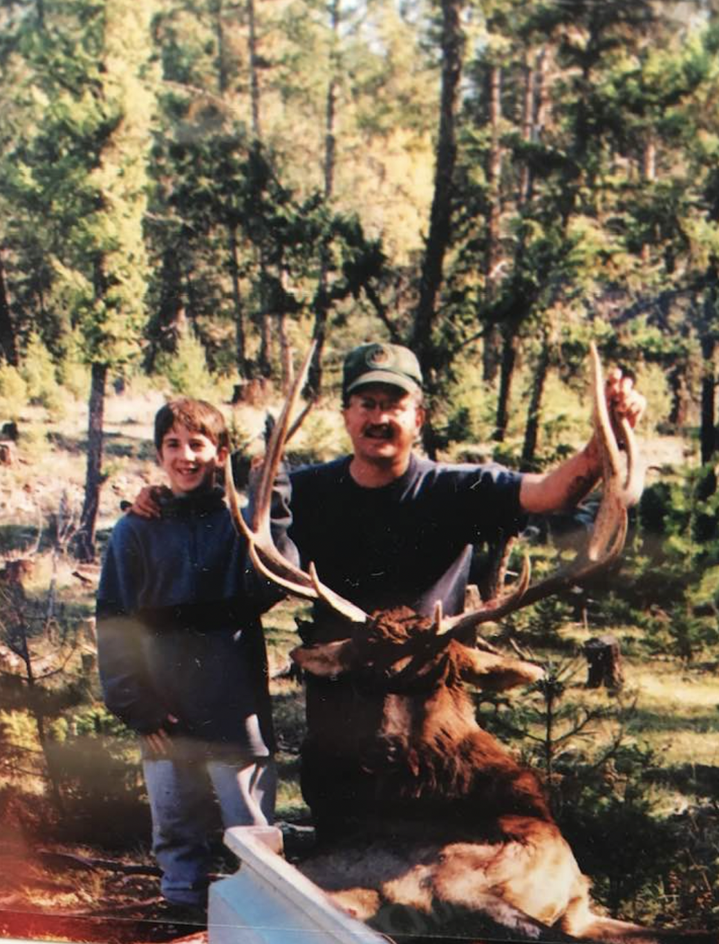 An elk hunter poses with an elk alongside his son. 