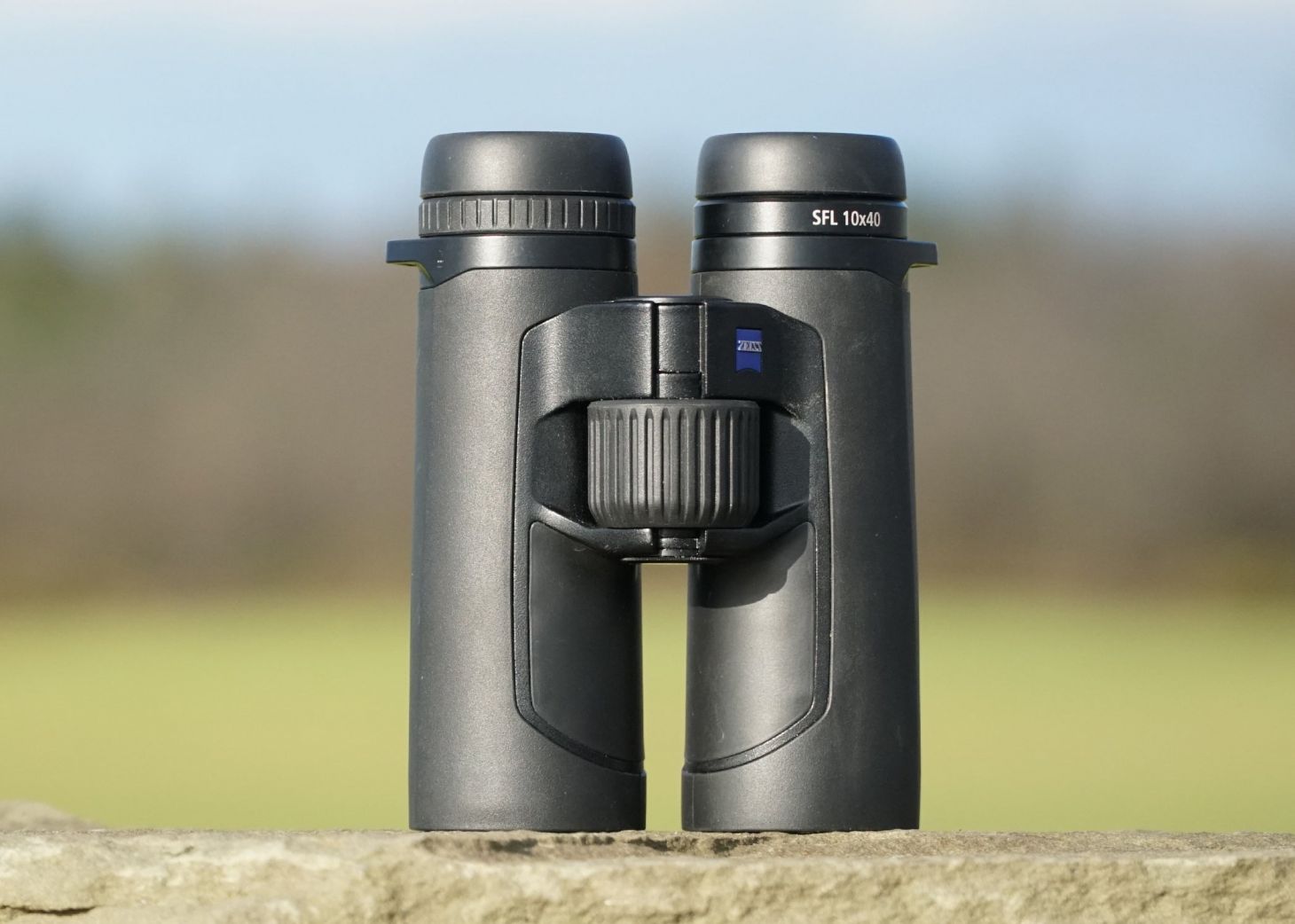 Zeiss SFL 10x40 binocular resting on a field stone, a green field in the backgound