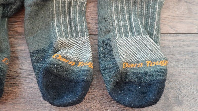 A close up of green and black Darn Tough socks sitting on a hardwood floor.