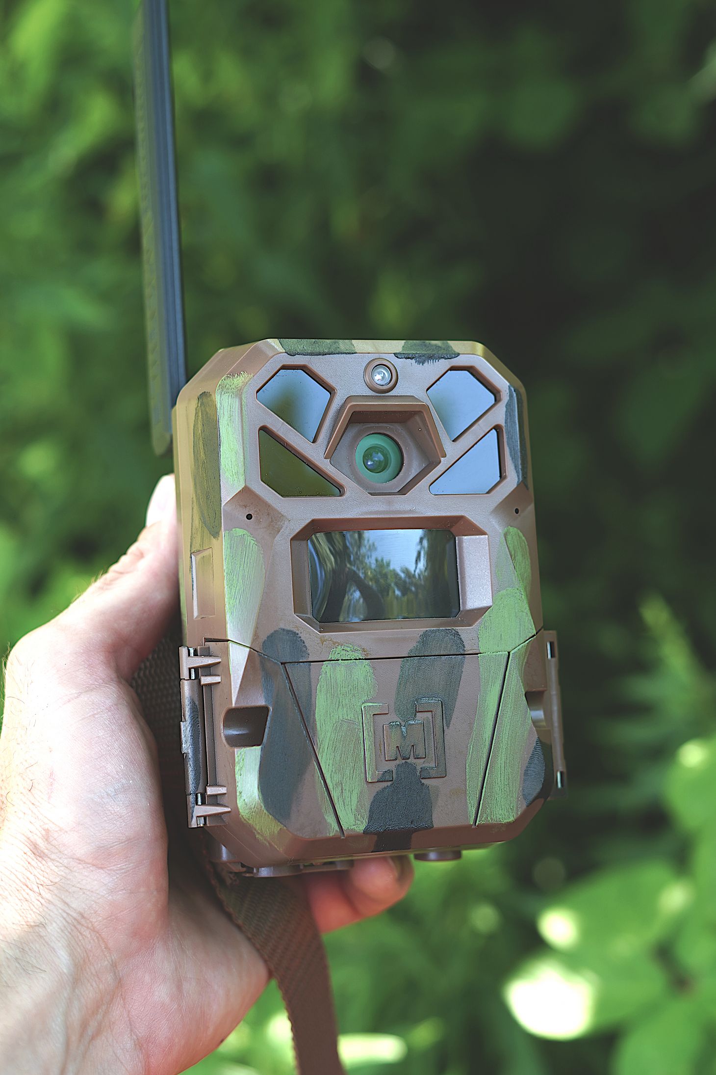 A hunter holds up a trail camera with camo facepaint on it. 