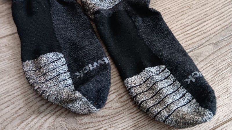 The bottom of a pair of black and gray Swiftwick trail socks on a hardwood floor.